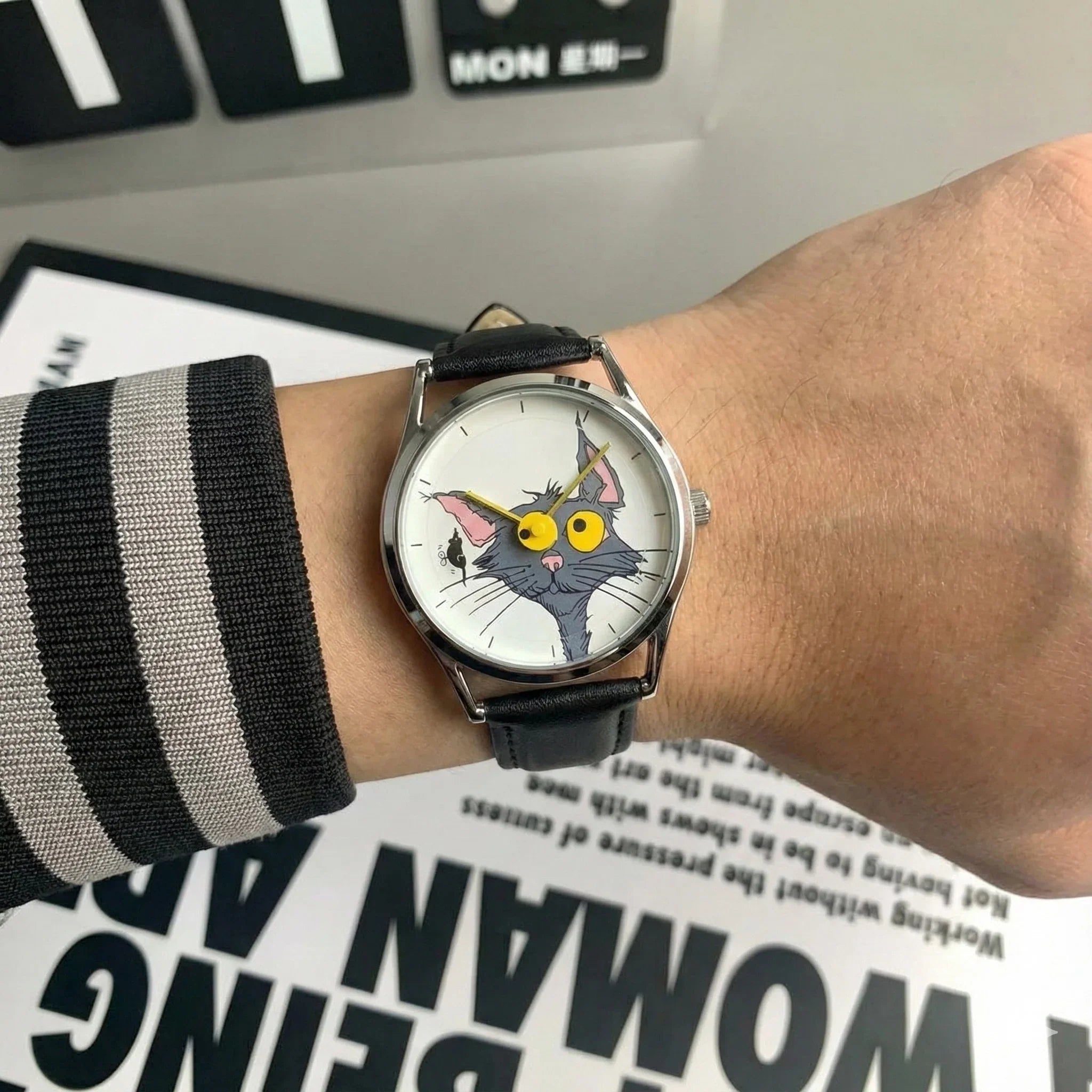 Wrist wearing a watch with a cat face design on a surface with text.